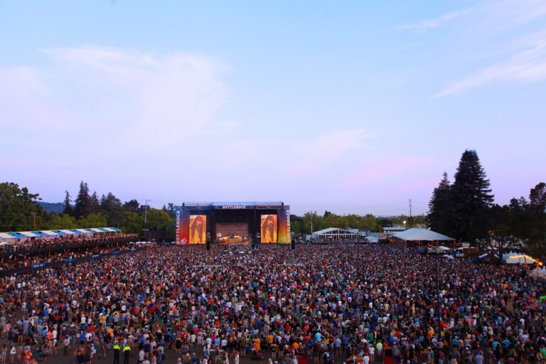 Slightly aerial view of BottleRock festival. The foreground is filled with people and a stage is seen in the distance.